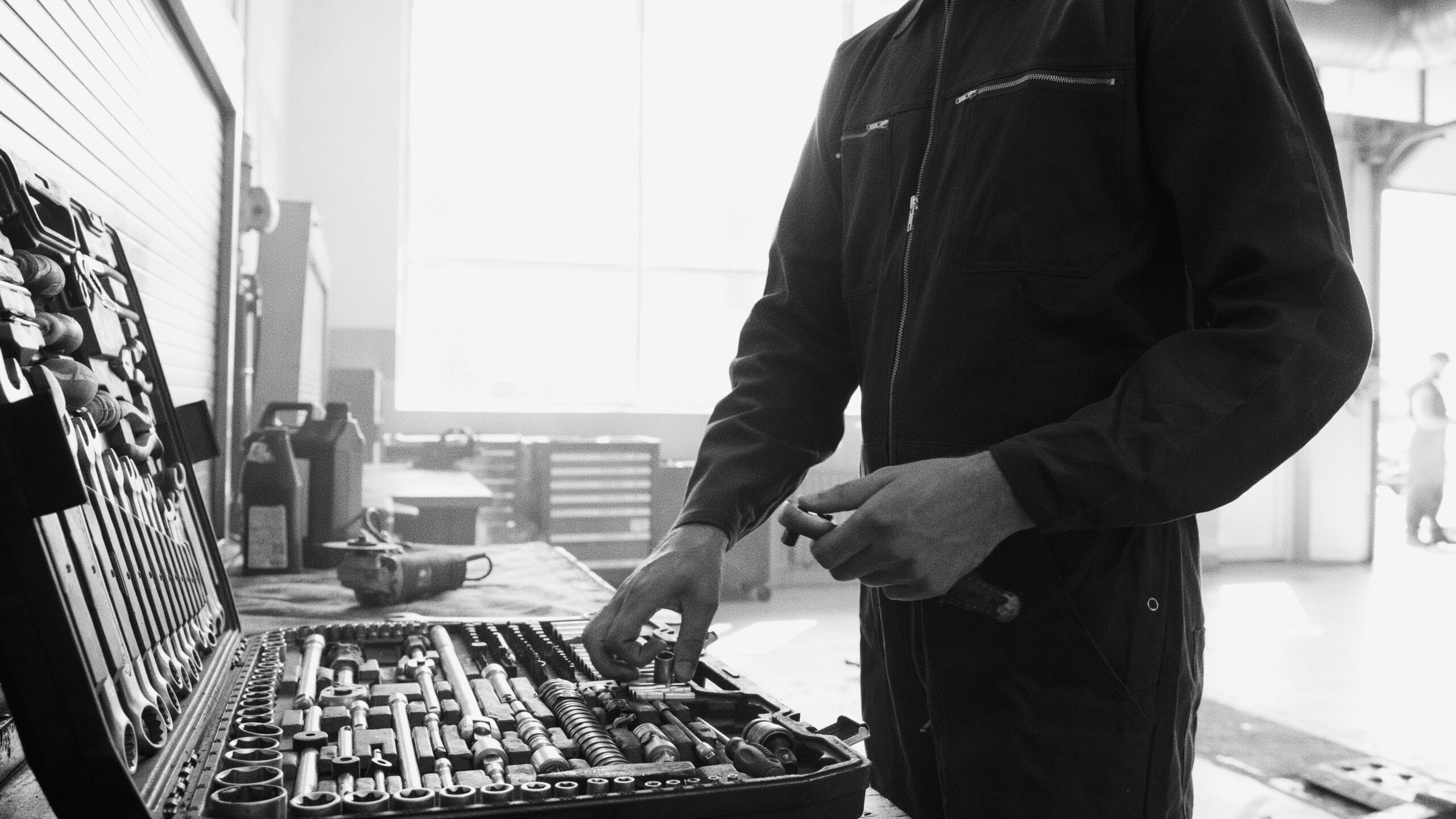 Grayscale Photo of Man in Black Overall Choosing a Tool in a Box